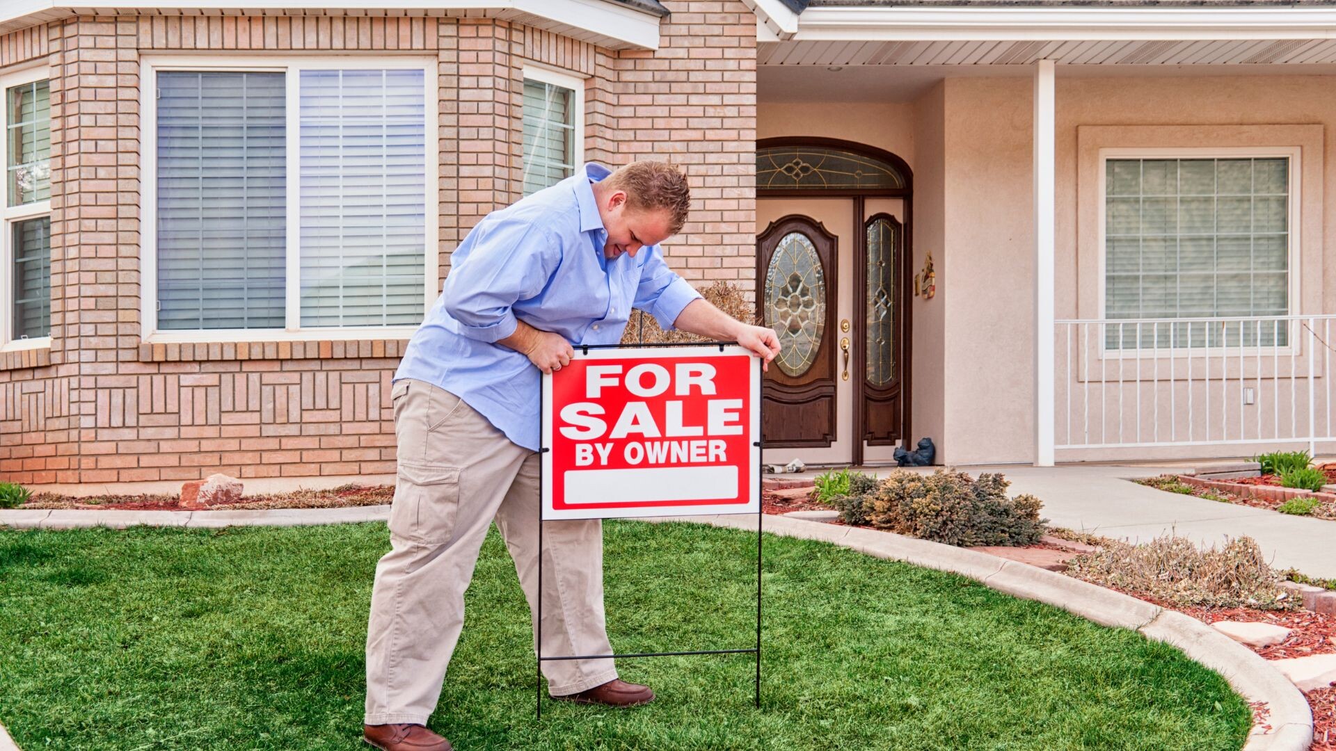 A man putting up a for sale sign in front of his house